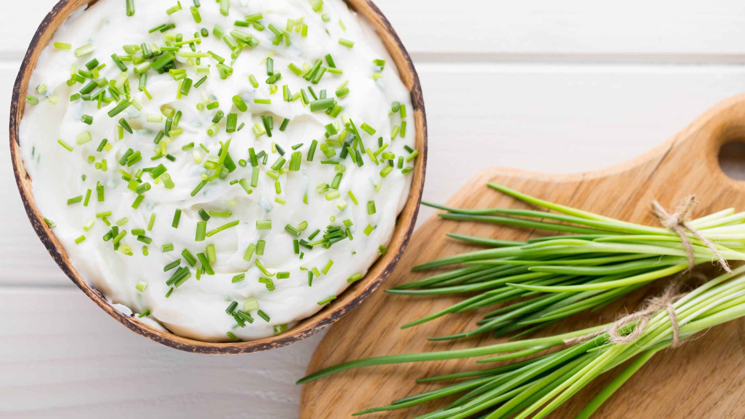 Bowl of cream cheese with green onions, dip sauce on wooden table.